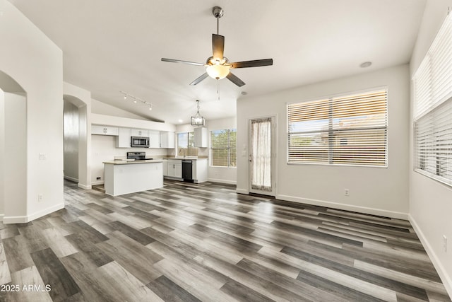 unfurnished living room featuring lofted ceiling, dark wood-style floors, arched walkways, baseboards, and ceiling fan