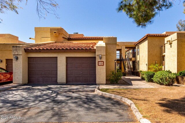 view of front of property with aphalt driveway, a tiled roof, stairs, stucco siding, and an attached garage