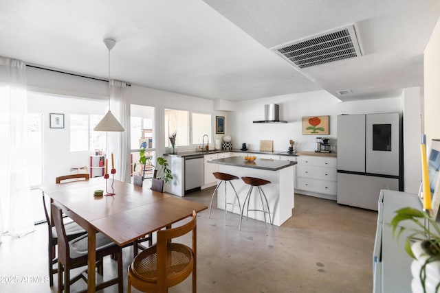 kitchen with appliances with stainless steel finishes, pendant lighting, white cabinets, a center island, and wall chimney exhaust hood