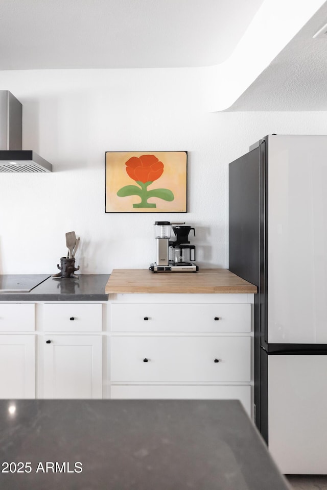 kitchen featuring white cabinetry, butcher block counters, fridge, black electric stovetop, and wall chimney exhaust hood