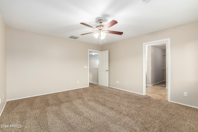 unfurnished bedroom featuring light carpet, a closet, ceiling fan, and a walk in closet