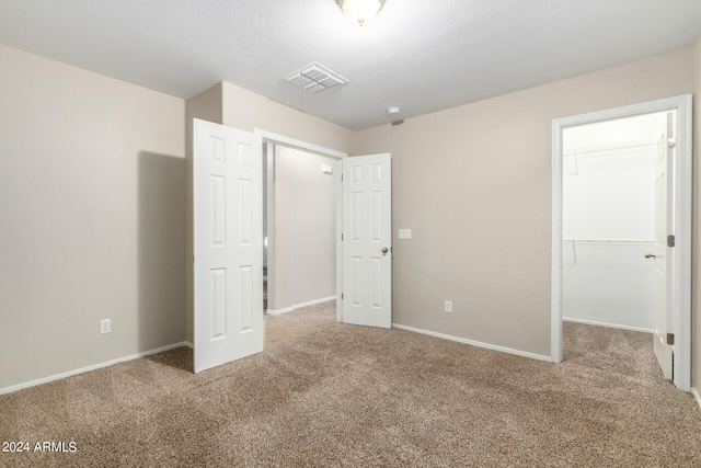 unfurnished bedroom with carpet floors, a textured ceiling, a walk in closet, and a closet