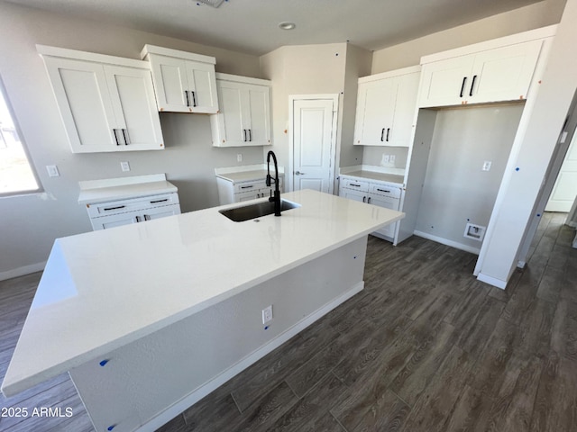 kitchen with light countertops, a sink, a center island with sink, and white cabinets