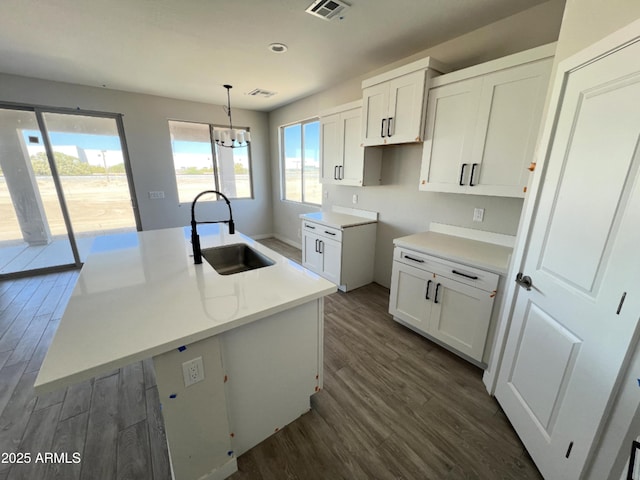 kitchen featuring a kitchen island with sink, light countertops, a sink, and decorative light fixtures