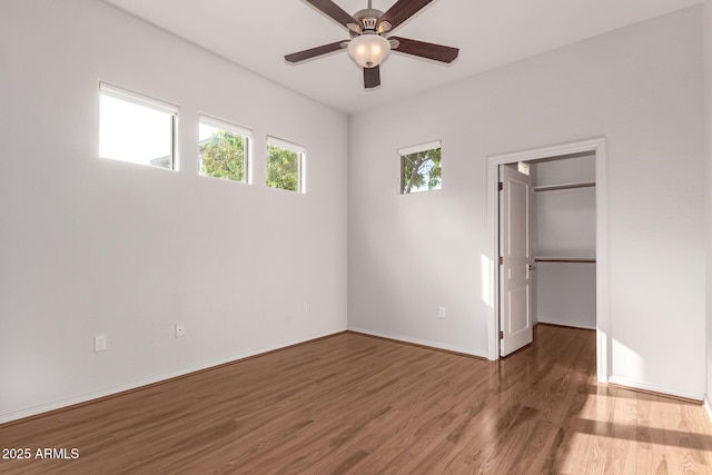 unfurnished bedroom featuring wood-type flooring, a spacious closet, and ceiling fan