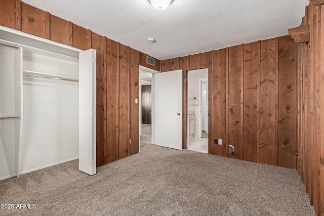 unfurnished bedroom featuring wood walls, light colored carpet, visible vents, a closet, and ensuite bath