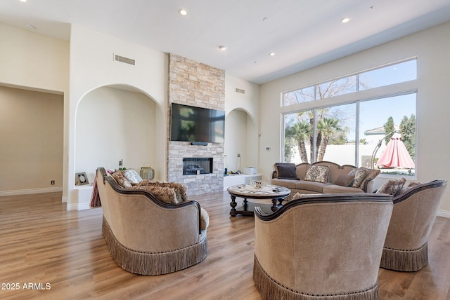 living room with a stone fireplace, visible vents, arched walkways, and light wood-type flooring