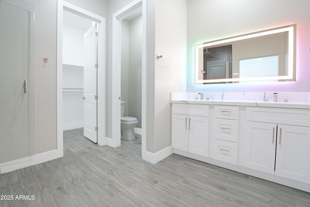 bathroom featuring toilet, double vanity, wood finished floors, a shower, and a sink