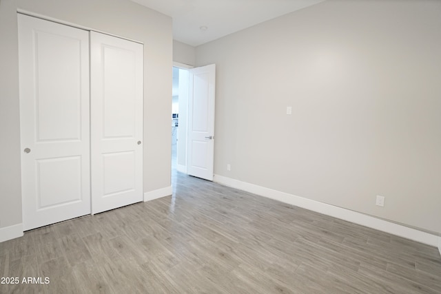 unfurnished bedroom with a closet, baseboards, and light wood finished floors