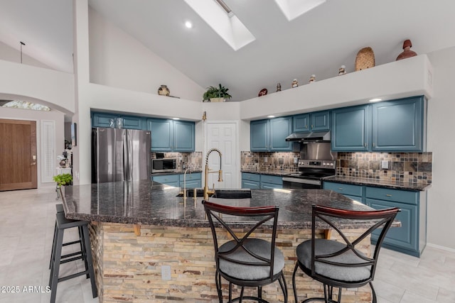 kitchen featuring a breakfast bar area, blue cabinetry, a skylight, under cabinet range hood, and appliances with stainless steel finishes