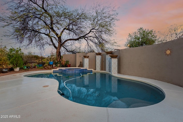 pool at dusk with a patio, a pool with connected hot tub, and fence