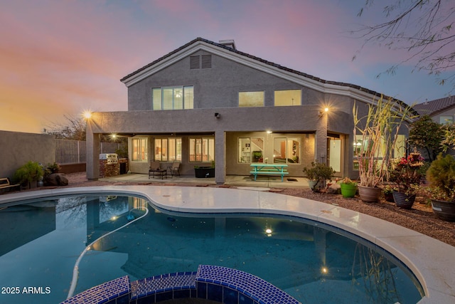 back of property at dusk with a patio area, fence, a pool with connected hot tub, and stucco siding