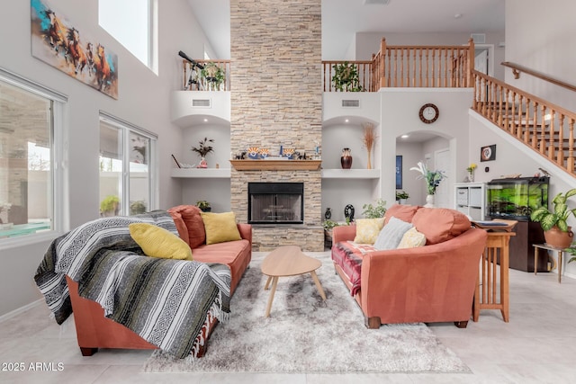 tiled living area featuring stairs, a stone fireplace, visible vents, and a towering ceiling