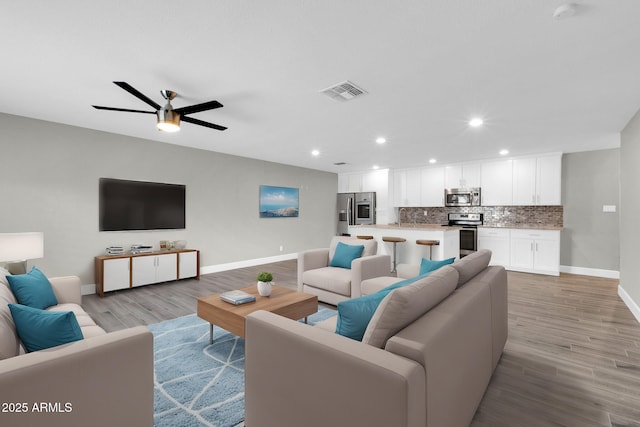 living room featuring recessed lighting, a ceiling fan, visible vents, baseboards, and light wood-type flooring