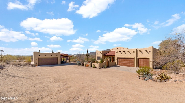 adobe home with stucco siding, an attached garage, and dirt driveway