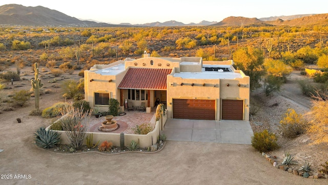 pueblo revival-style home featuring stucco siding, driveway, a mountain view, a garage, and a tiled roof