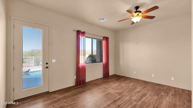 empty room featuring visible vents, a ceiling fan, and wood finished floors