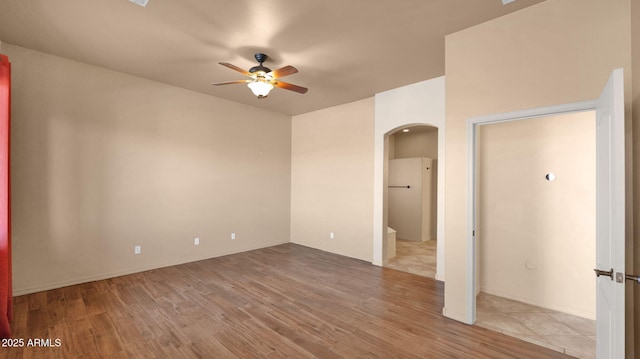 empty room with arched walkways, a ceiling fan, and wood finished floors