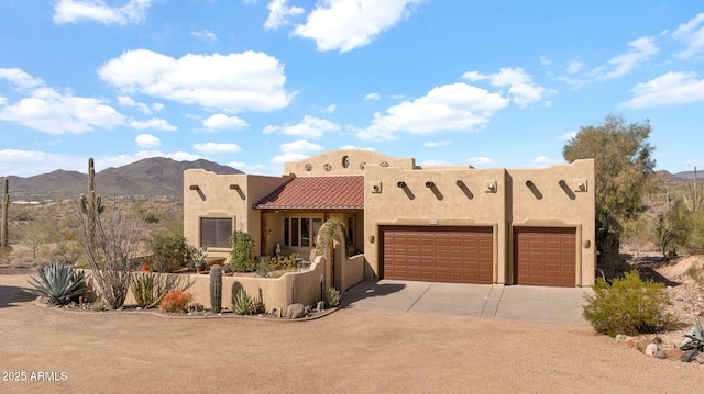 adobe home with a tile roof, concrete driveway, stucco siding, a garage, and a mountain view