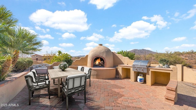 view of patio with grilling area, a warm lit fireplace, outdoor dining space, an outdoor kitchen, and a mountain view