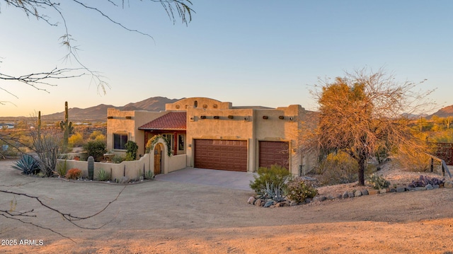 pueblo revival-style home with stucco siding, driveway, fence, a mountain view, and an attached garage