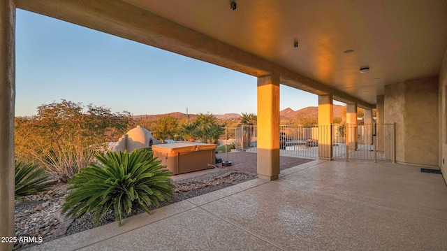 view of patio with fence, a mountain view, and a hot tub