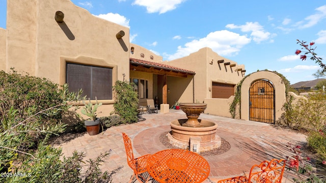 exterior space with fence, a tile roof, stucco siding, a patio area, and a gate