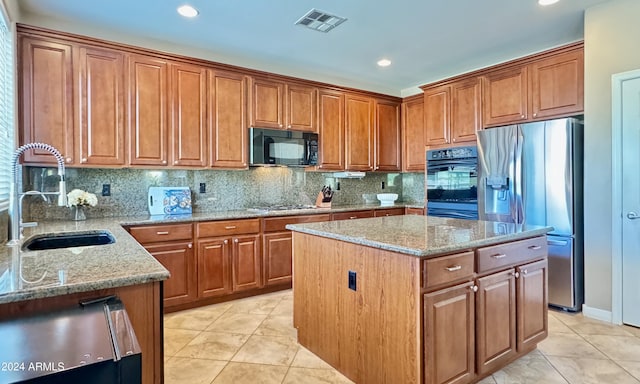 kitchen with black appliances, a kitchen island, light stone countertops, and sink