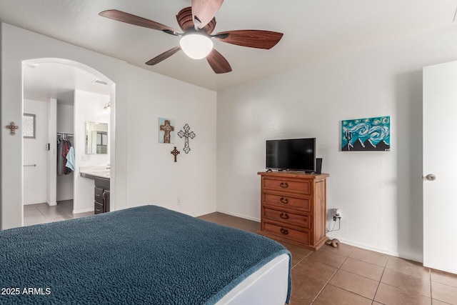 bedroom featuring tile patterned floors, arched walkways, ceiling fan, baseboards, and connected bathroom