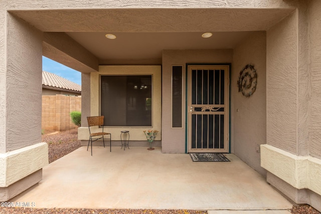 entrance to property with stucco siding, fence, and a patio