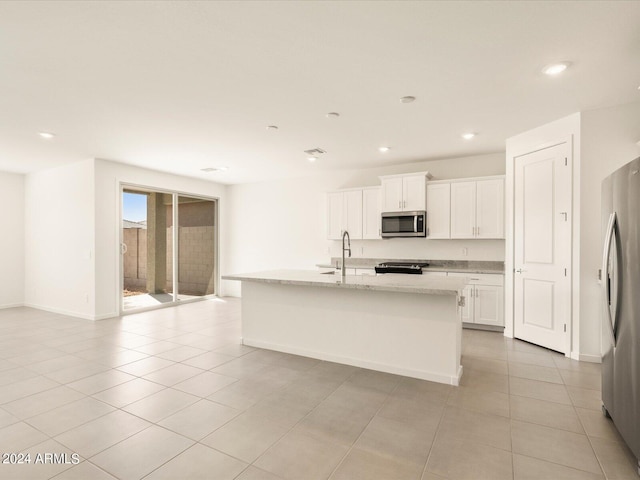 kitchen with light stone countertops, an island with sink, white cabinets, and appliances with stainless steel finishes