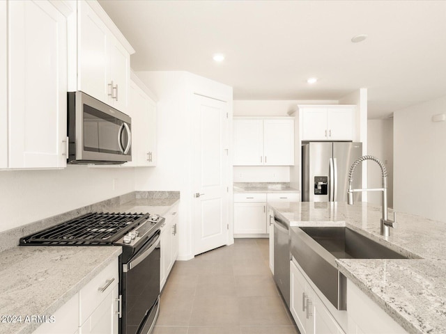 kitchen featuring sink, white cabinetry, stainless steel appliances, light stone countertops, and light tile patterned flooring