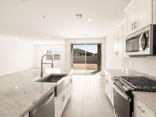 kitchen with sink, light stone counters, light tile patterned floors, appliances with stainless steel finishes, and white cabinets