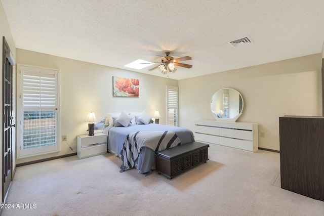 carpeted bedroom with a textured ceiling, ceiling fan, multiple windows, and a skylight