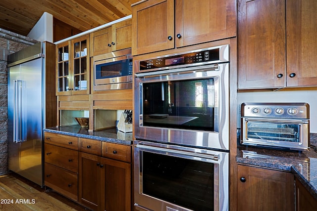 kitchen featuring dark wood-type flooring, wood ceiling, dark stone counters, and built in appliances