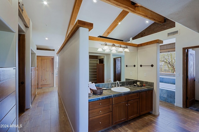 bathroom with hardwood / wood-style flooring, a relaxing tiled tub, vanity, and lofted ceiling with beams