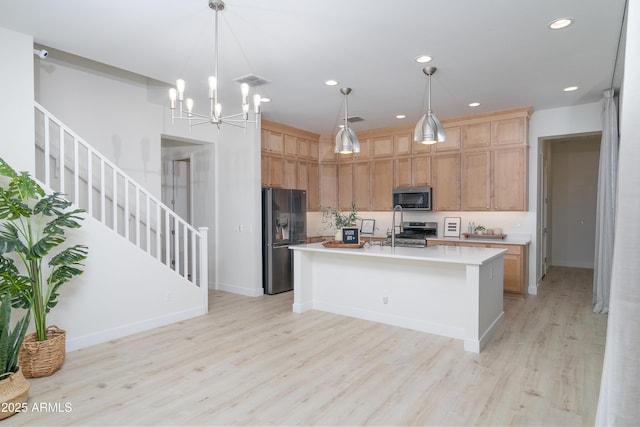 kitchen with pendant lighting, light hardwood / wood-style floors, stainless steel appliances, and an island with sink