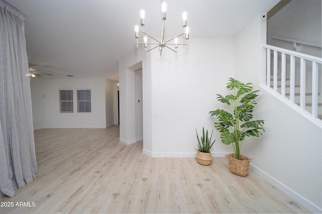 empty room with ceiling fan with notable chandelier and light wood-type flooring