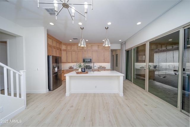 kitchen featuring a center island with sink, light hardwood / wood-style flooring, appliances with stainless steel finishes, decorative light fixtures, and a chandelier