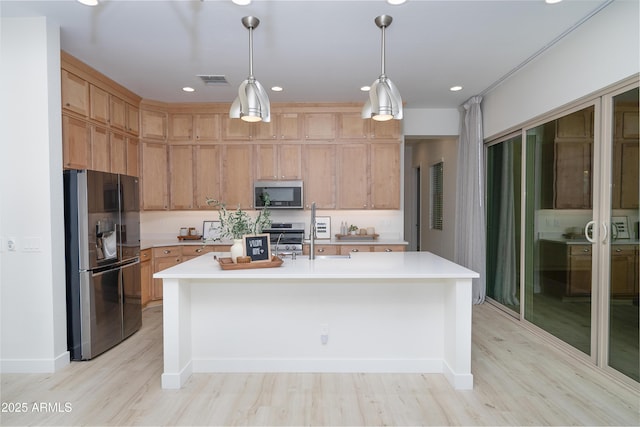 kitchen with appliances with stainless steel finishes, decorative light fixtures, a kitchen island with sink, and light hardwood / wood-style floors