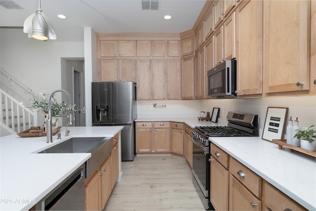 kitchen with sink, light brown cabinets, hanging light fixtures, stainless steel appliances, and light hardwood / wood-style floors