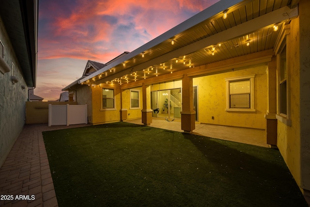 back house at dusk featuring a lawn and a patio area