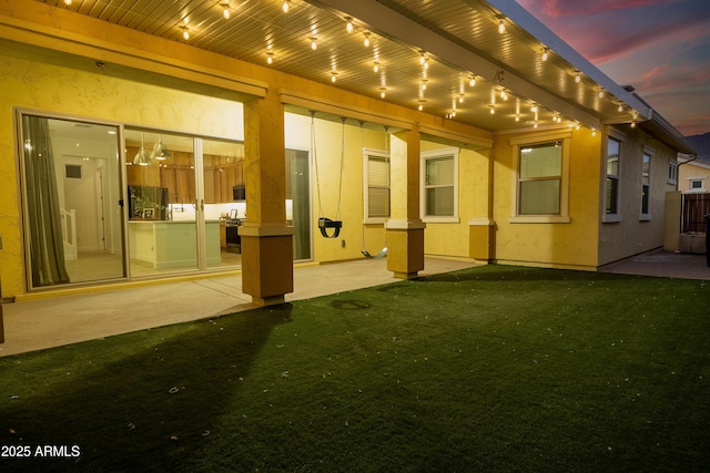 back house at dusk featuring a yard and a patio area