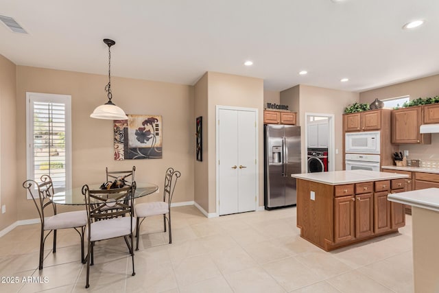 kitchen featuring decorative light fixtures, light tile patterned floors, a kitchen island, white appliances, and washer / clothes dryer