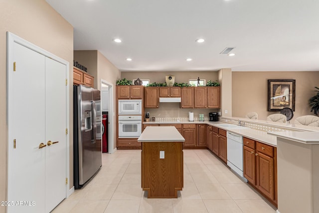 kitchen with light tile patterned flooring, sink, a center island, kitchen peninsula, and white appliances