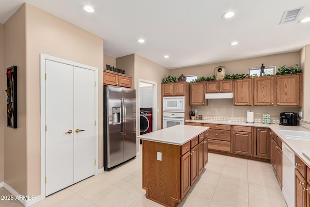 kitchen with washer / dryer, a kitchen island, light tile patterned floors, and white appliances