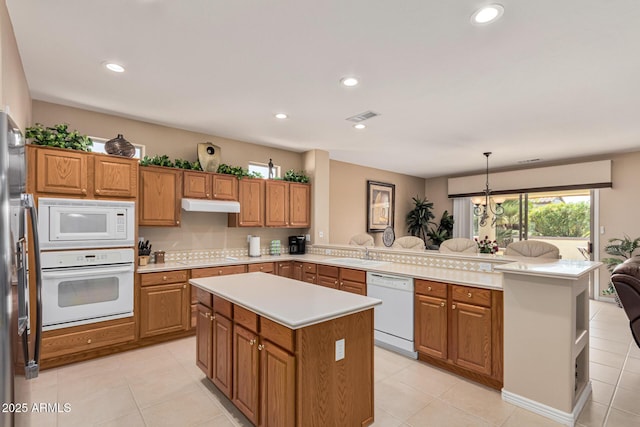 kitchen with light tile patterned flooring, a center island, hanging light fixtures, kitchen peninsula, and white appliances