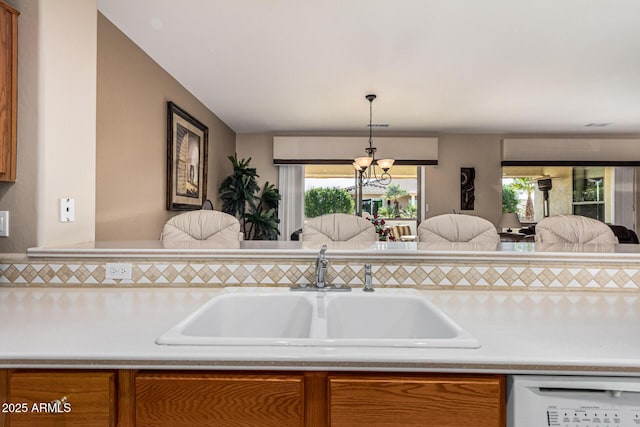 kitchen featuring white dishwasher, sink, pendant lighting, and an inviting chandelier