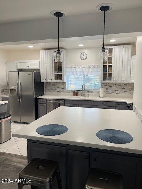 kitchen with stainless steel appliances, white cabinetry, hanging light fixtures, light wood-type flooring, and decorative backsplash