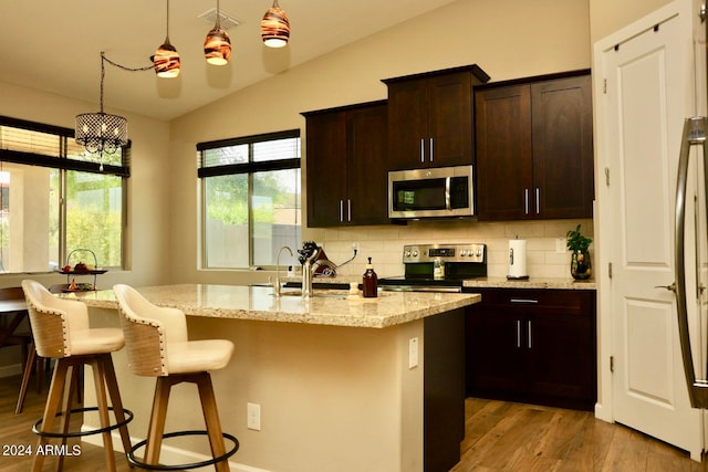 kitchen featuring decorative light fixtures, vaulted ceiling, stainless steel appliances, tasteful backsplash, and light wood-type flooring